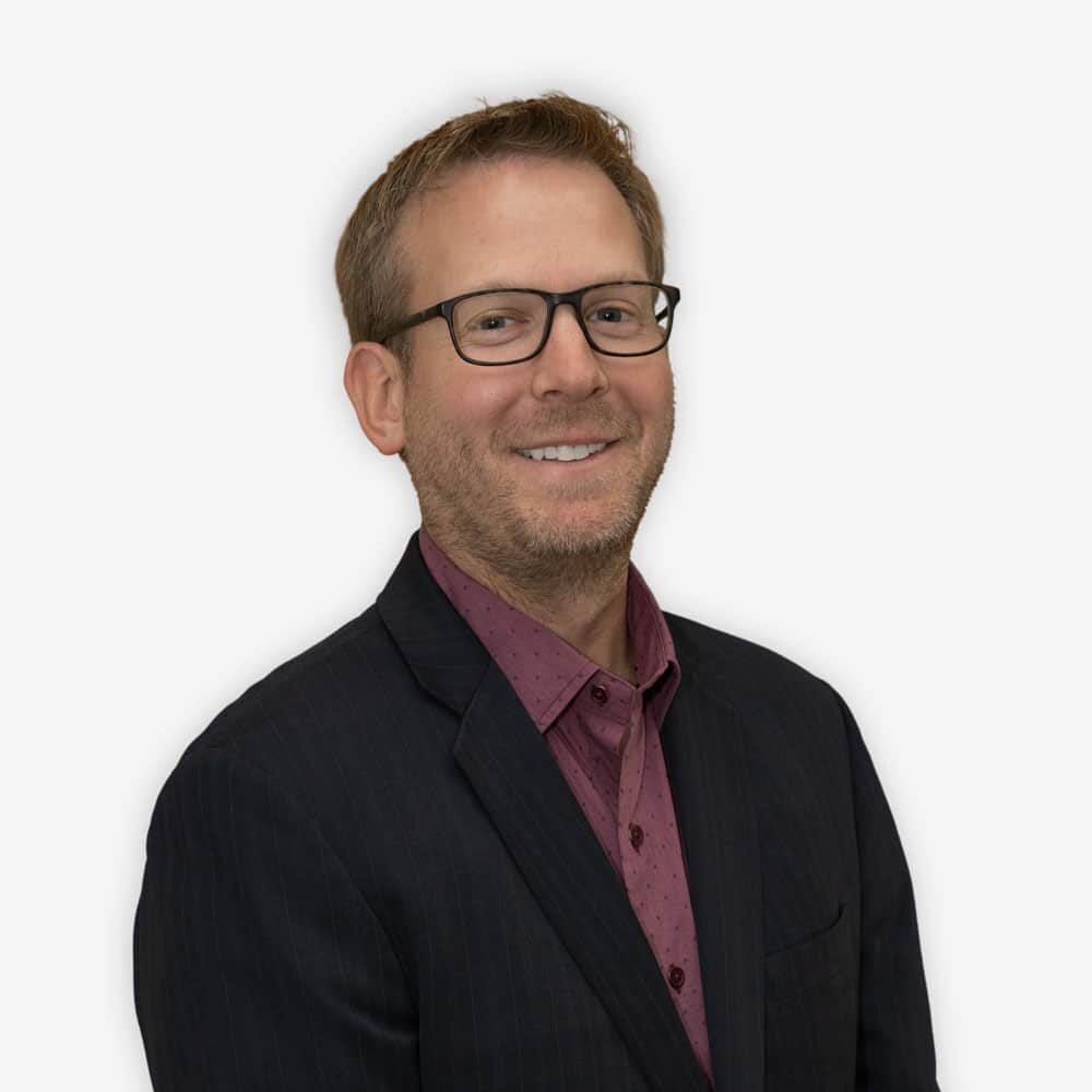 Dr. Sean Ormond of Atlas Pain Specialists smiling in a dark suit with purple shirt on a white background