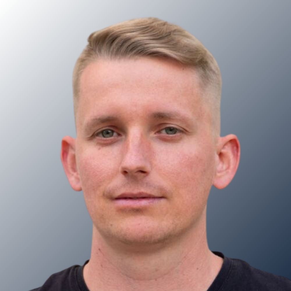 2 portrait of Caleb Riutta with a grey wall in the background.